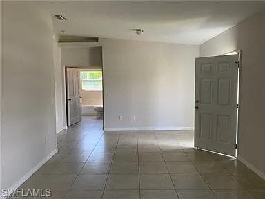 Tiled spare room featuring visible vents and baseboards