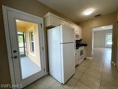 Kitchen featuring visible vents, baseboards, light tile patterned flooring, white cabinets, and white appliances