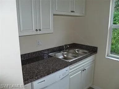Kitchen featuring a sink, baseboards, white dishwasher, and white cabinetry