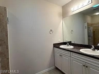 Full bath featuring a sink, baseboards, double vanity, and a tile shower