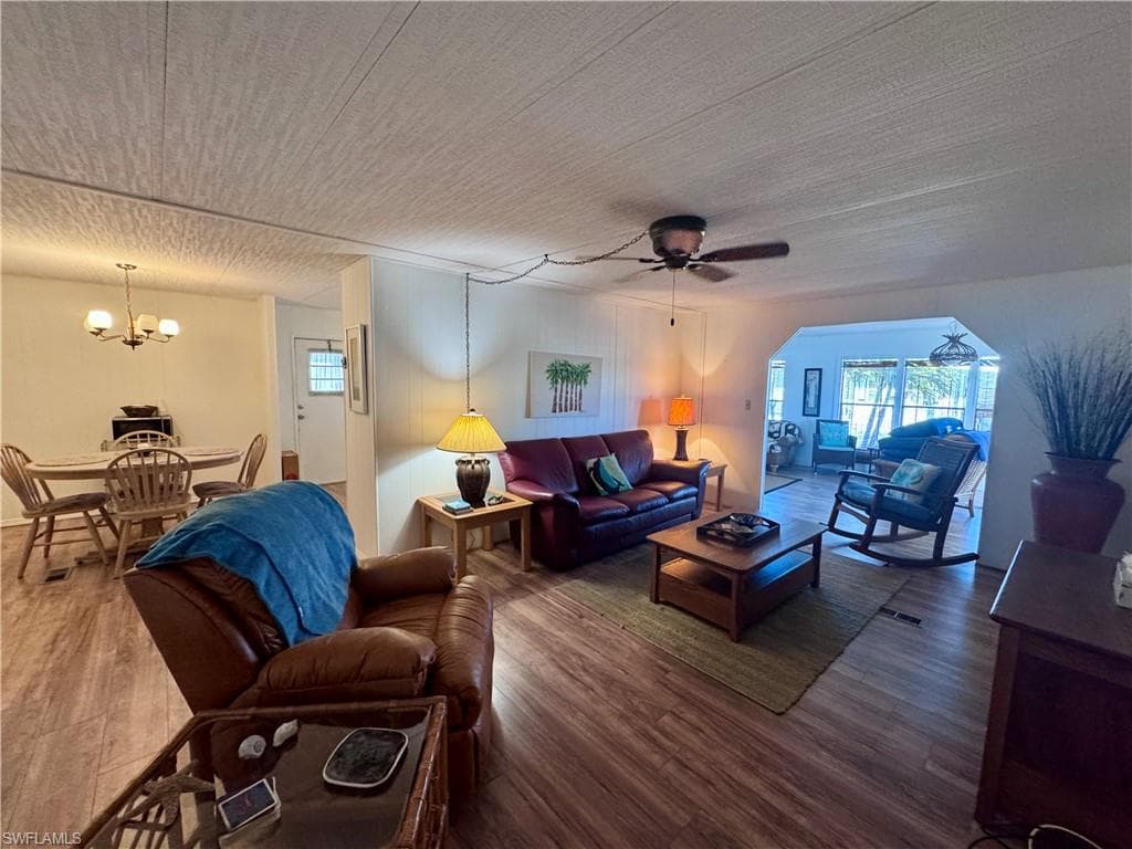 Living area featuring ceiling fan with notable chandelier, a textured ceiling, and wood finished floors