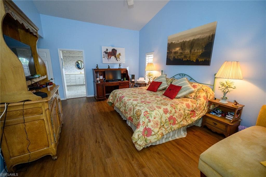 Bedroom with high vaulted ceiling, ensuite bath, dark wood finished floors, and a ceiling fan