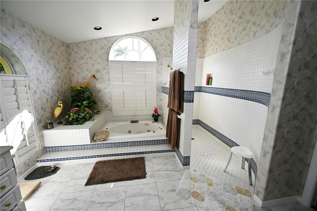 Bathroom with a tub with jets, marble finish floor, a walk in shower, and dual sinks.