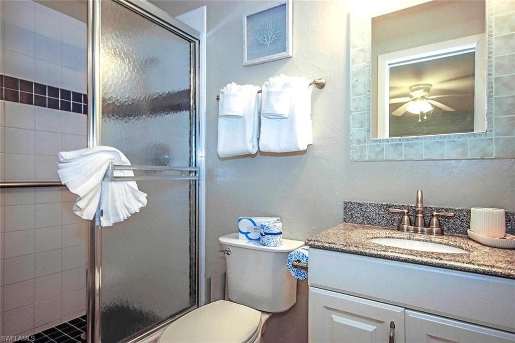 Full bath featuring vanity, a shower stall, toilet, and a ceiling fan