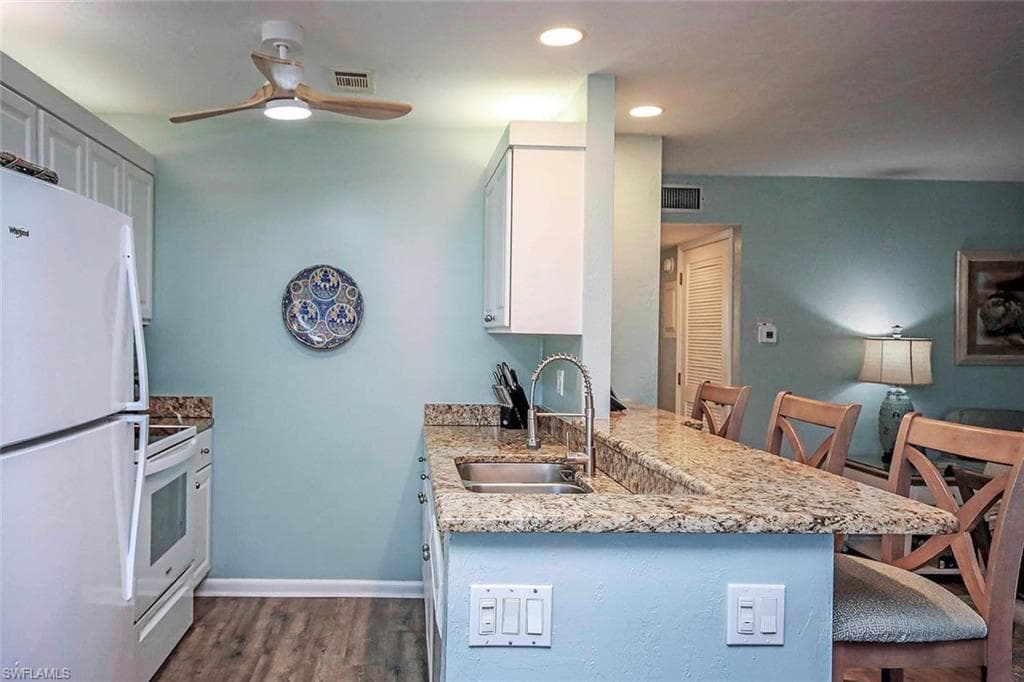 Kitchen featuring a sink, white appliances, a peninsula, ceiling fan, and dark wood-style flooring