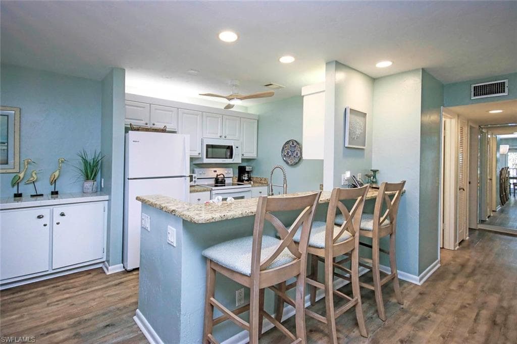 Kitchen featuring white appliances, visible vents, a peninsula, recessed lighting, and dark wood-type flooring