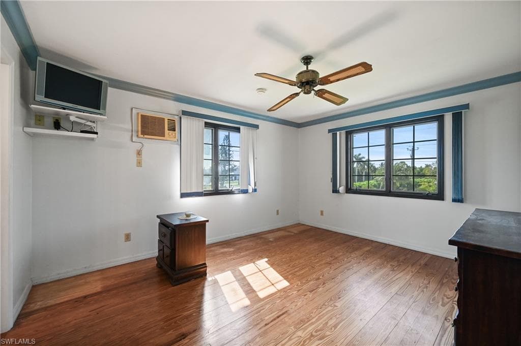 Unfurnished room featuring wood finished floors, ceiling fan, ornamental molding, and a wall unit AC