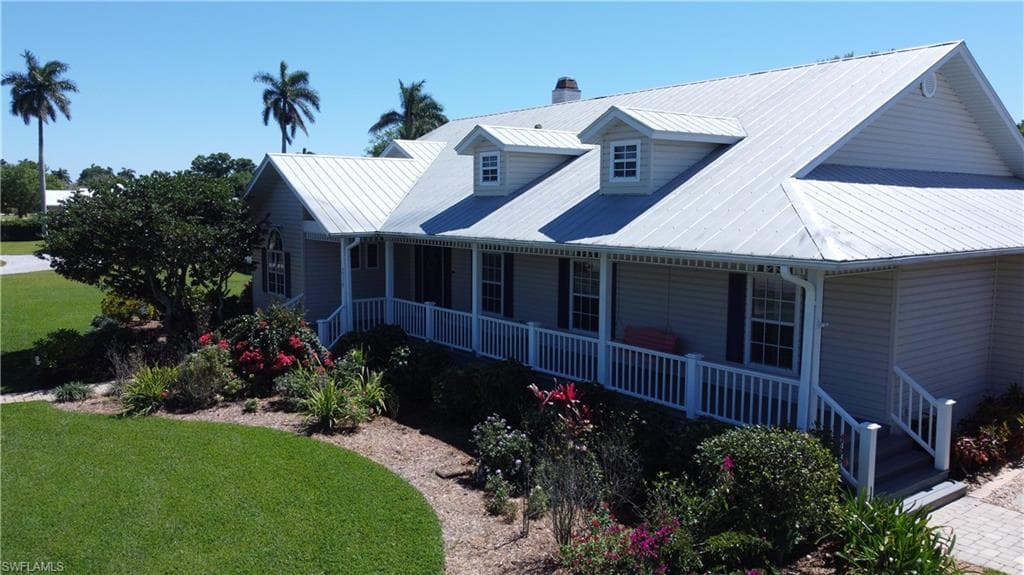 View of front of house featuring covered porch, a chimney, and a front yard