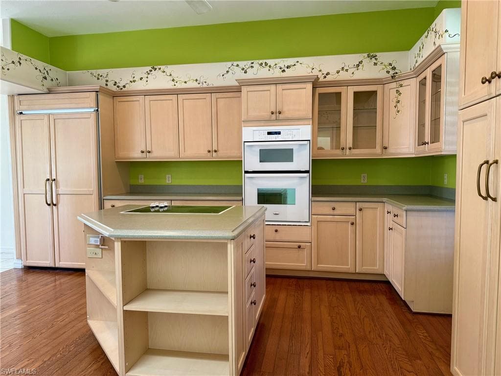 Kitchen with paneled fridge, open shelves, double oven, black electric stovetop, and dark wood-style flooring