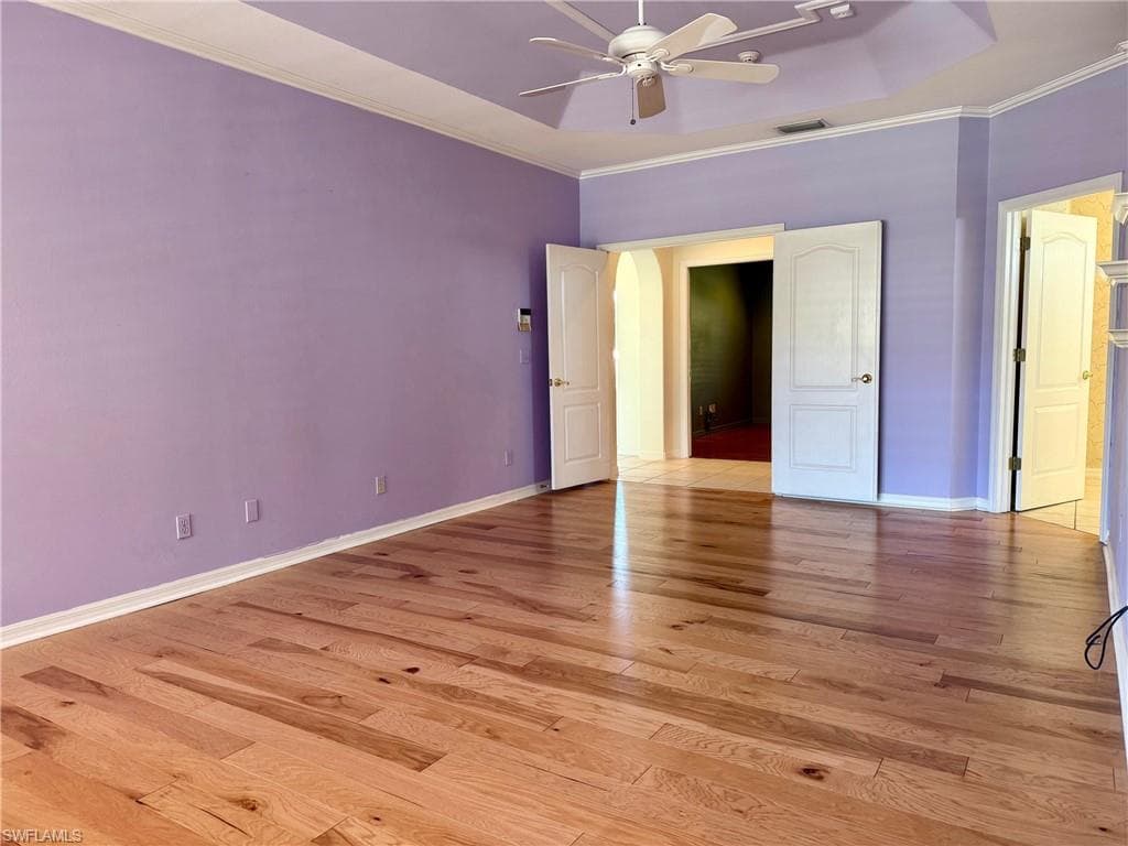 Unfurnished bedroom featuring visible vents, baseboards, arched walkways, crown molding, and light wood-type flooring