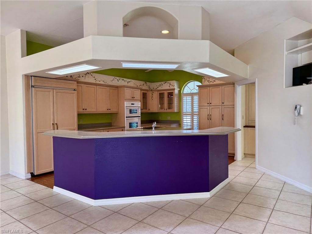 Kitchen featuring a spacious island, white double oven, glass insert cabinets, baseboards, and light tile patterned floors