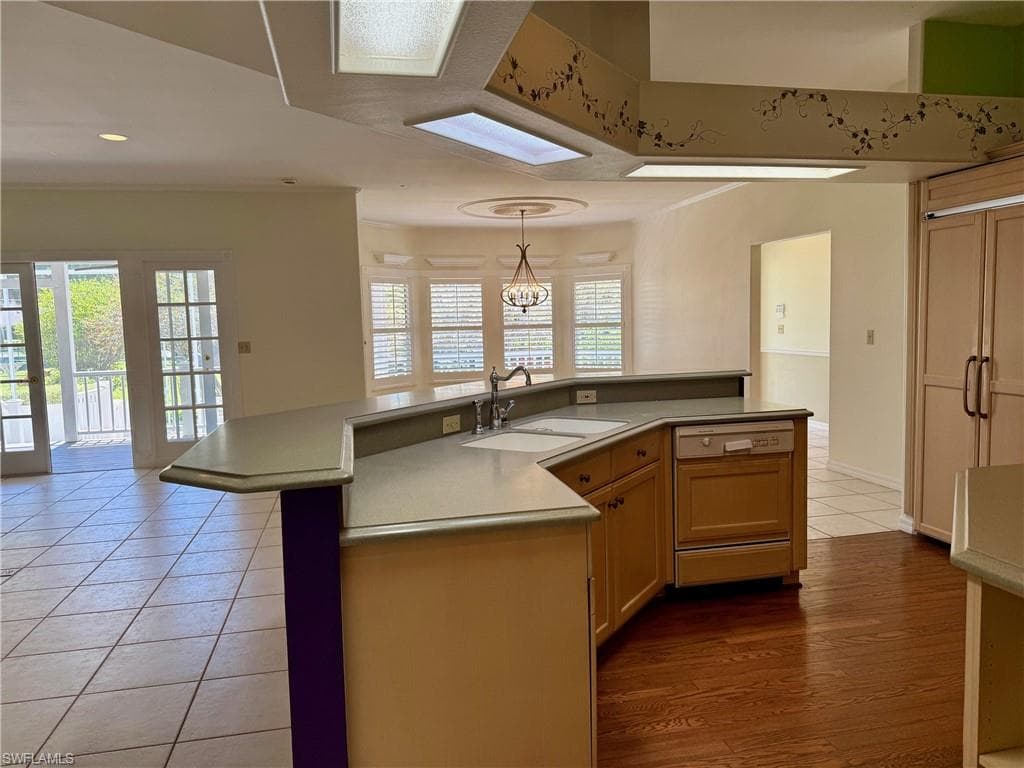 Kitchen with light tile patterned floors, a kitchen island with sink, a sink, dishwasher, and decorative light fixtures