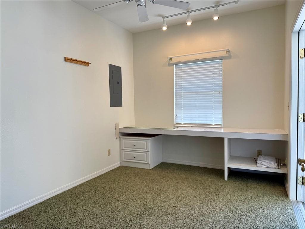 Unfurnished office with a ceiling fan, electric panel, built in desk, carpet floors, and baseboards