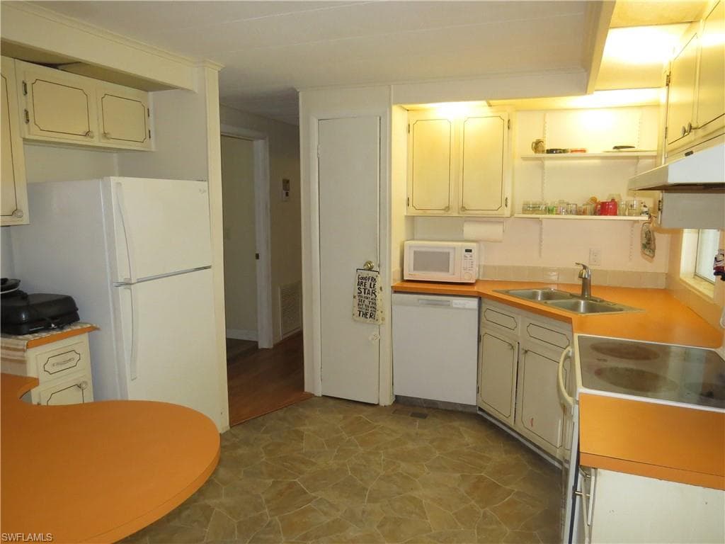 Kitchen featuring visible vents, under cabinet range hood, a sink, white appliances, and light countertops