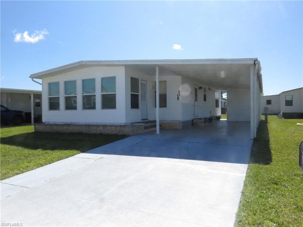 Manufactured / mobile home featuring an attached carport, concrete driveway, and a front lawn