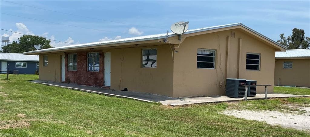 Rear view of property with a lawn, metal roof, cooling unit, and stucco siding