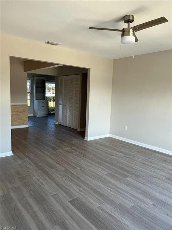 Unfurnished room featuring baseboards, visible vents, ceiling fan, and dark wood-style flooring