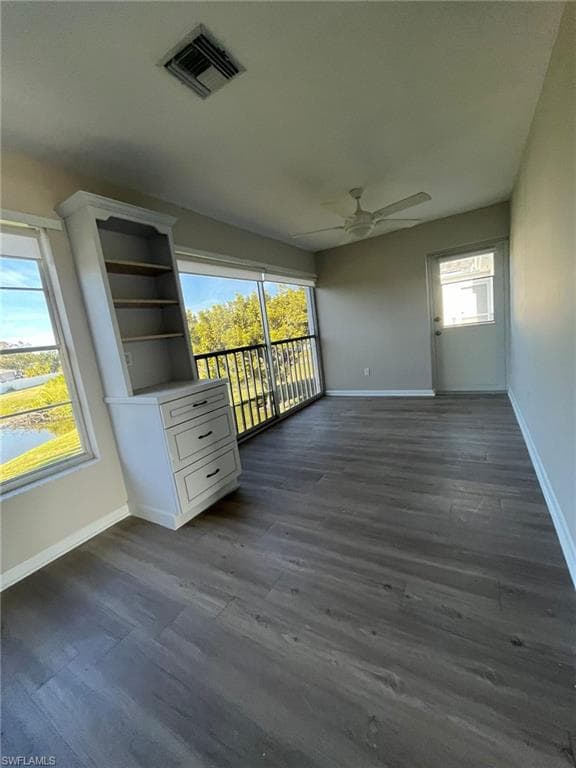 Unfurnished room with baseboards, dark wood-style floors, visible vents, and a ceiling fan