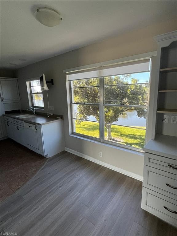 Kitchen featuring a water view, white cabinets, baseboards, dark wood finished floors, and a sink