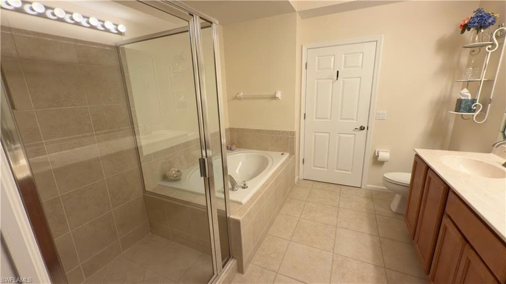 Bathroom featuring tile patterned flooring, double vanity, toilet, a shower stall, and a garden tub