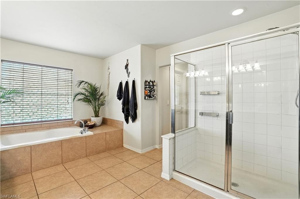 Luxurious primary bathroom with dual vanities, abundant counter space, and elegant dark cabinetry. A large soaking tub beneath a bright window offers a serene retreat, while the separate walk-in shower adds convenience. Warm tile flooring and stylish lighting create a spa-like ambiance, perfect for unwinding after a long day. This spacious en-suite blends comfort and function, making it an inviting highlight of this beautiful Southwest Florida home