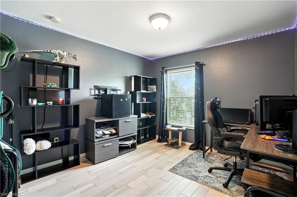 Versatile bedroom or home office with sleek dark gray walls, wood-look flooring, and a large window bringing in natural light. Ample space for desks, shelving, or creative setups makes it perfect for work-from-home, gaming, or hobbies. LED accent lighting adds a modern touch, while the neutral palette allows for easy personalization.