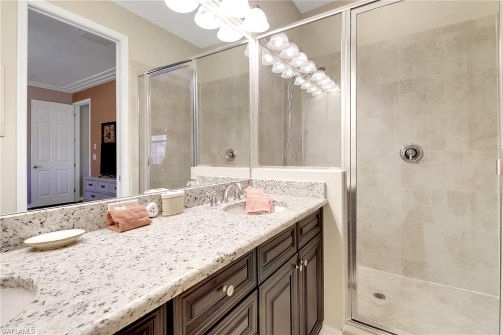 Full bath with a sink, a shower stall, an inviting chandelier, and double vanity