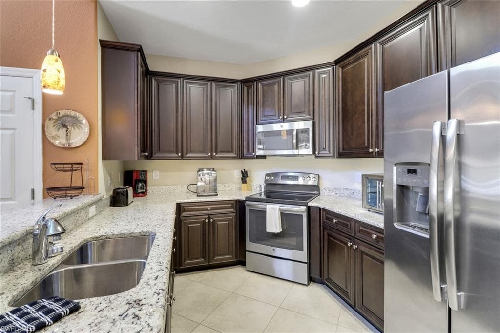 Kitchen with light stone countertops, dark brown cabinetry, light tile patterned flooring, a sink, and stainless steel appliances