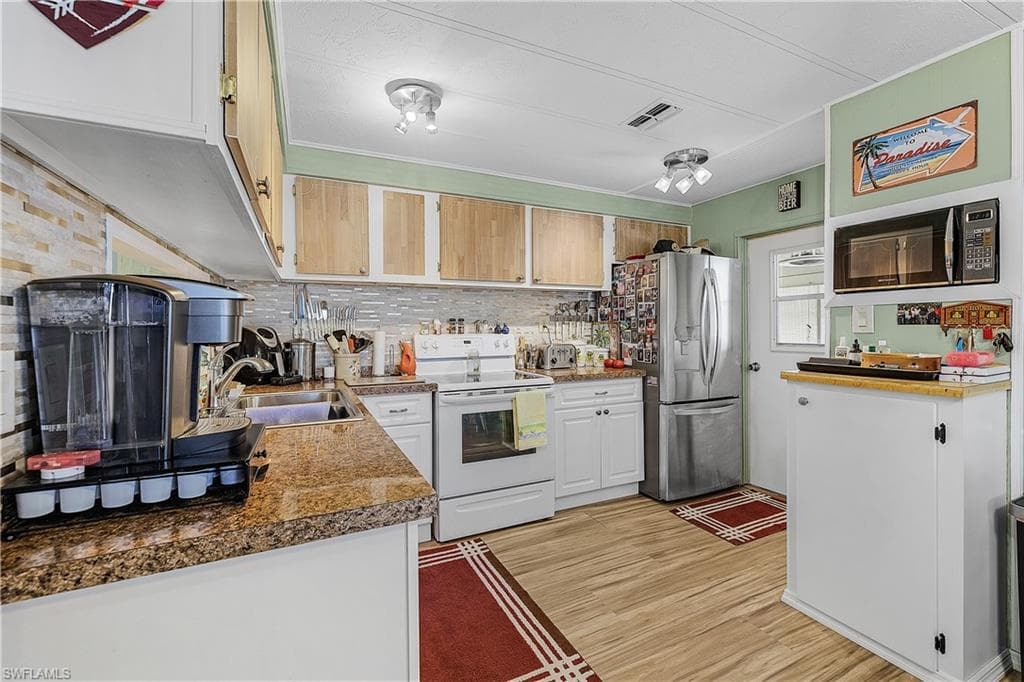 Kitchen with visible vents, stainless steel refrigerator with ice dispenser, a sink, light wood-style floors, and white electric range oven