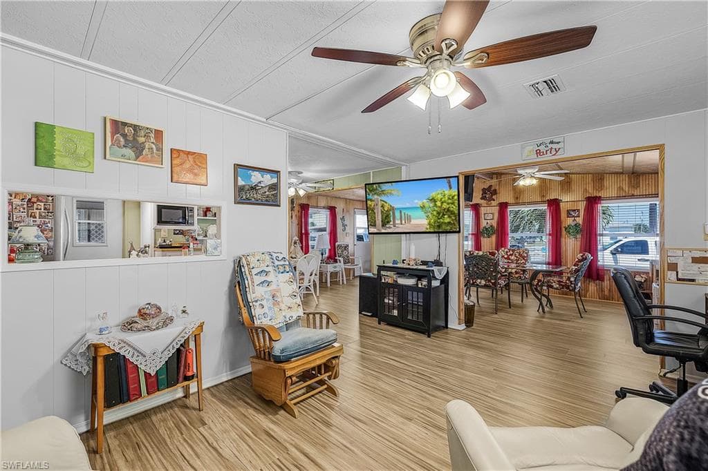 Living room with visible vents, ceiling fan, wood finished floors, and wood walls