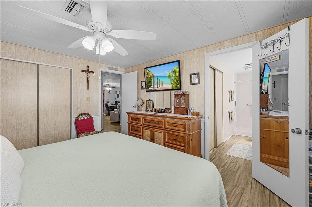 Bedroom with visible vents, a closet, ceiling fan, wood finished floors, and wood walls