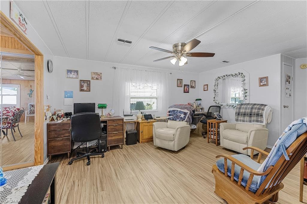 Office area with light wood finished floors, visible vents, a ceiling fan, and a healthy amount of sunlight