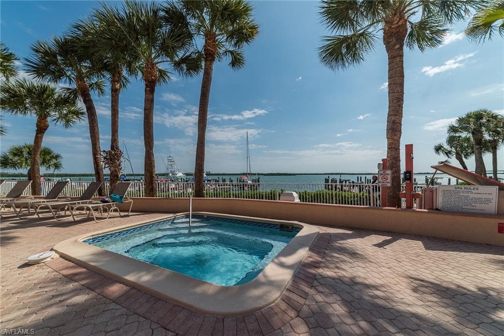 View of swimming pool with fence, a hot tub, and a water view
