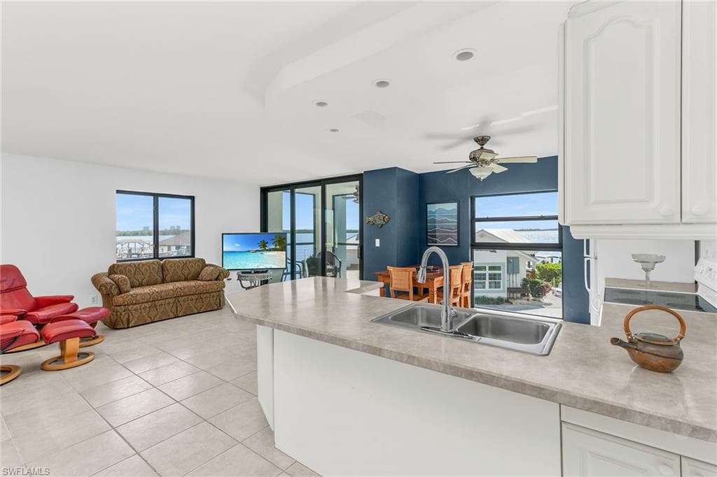 Kitchen with light tile patterned floors, a sink, open floor plan, a peninsula, and white cabinetry