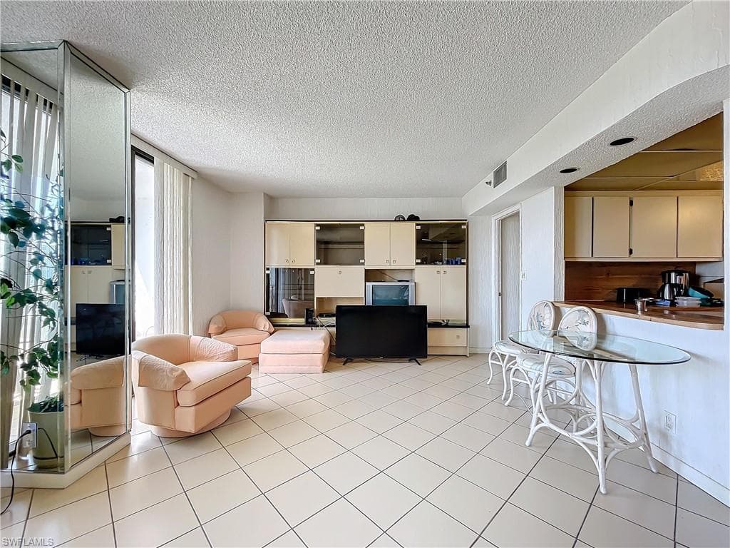 Living area with a textured ceiling, light tile patterned flooring, and visible vents