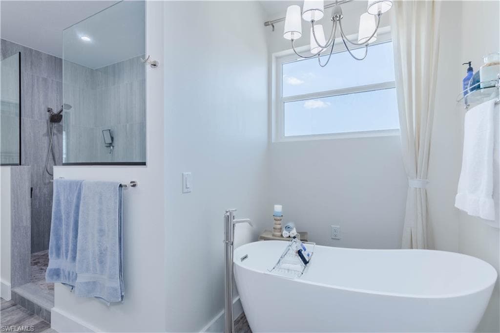 Bathroom featuring a soaking tub, a notable chandelier, and a walk in shower