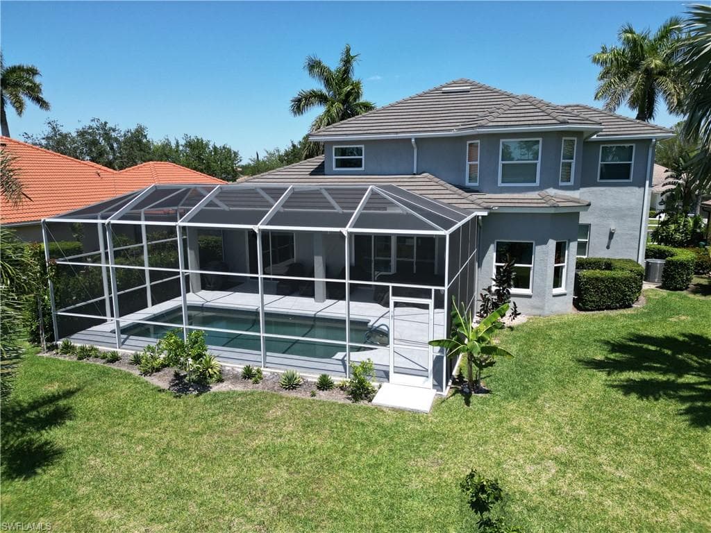 Back of house featuring an outdoor pool, a tiled roof, a yard, stucco siding, and a lanai