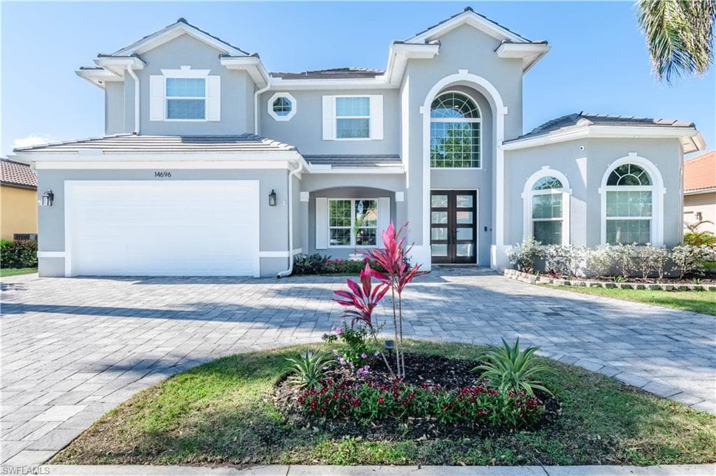 Traditional-style home with a tiled roof, stucco siding, french doors, decorative circular driveway with pavers, and a garage