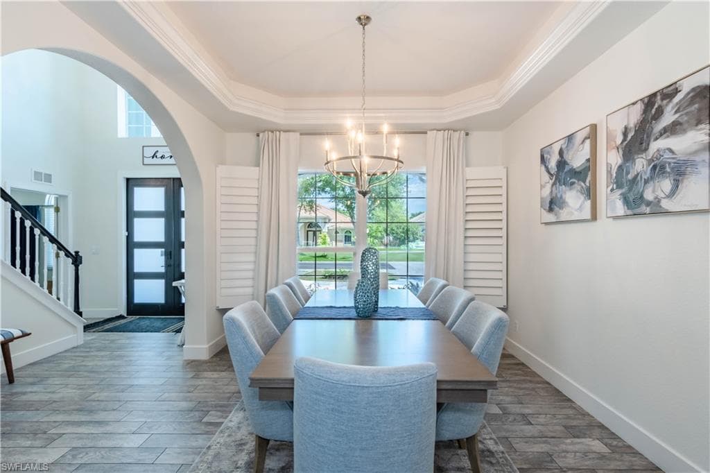 Dining space with arched walkways, a notable chandelier, a raised ceiling, and a healthy amount of sunlight