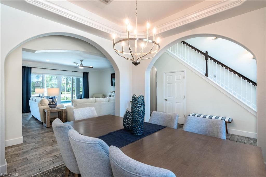 Dining room featuring arched walkways, baseboards, ceiling fan with notable chandelier and crown molding