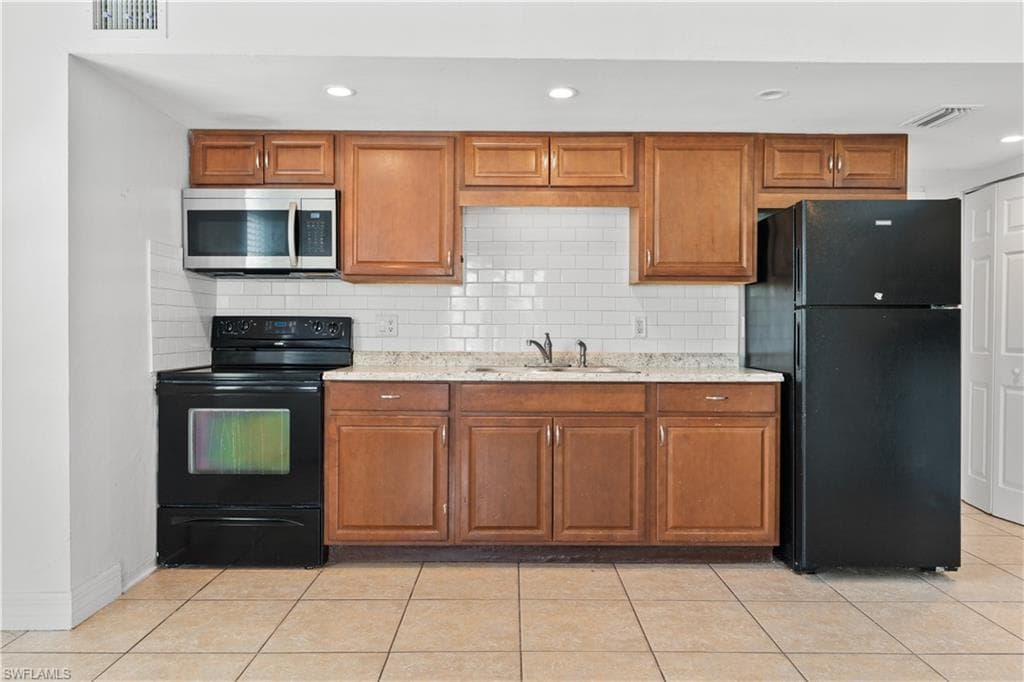 Kitchen with brown cabinets, visible vents, a sink, and black appliances