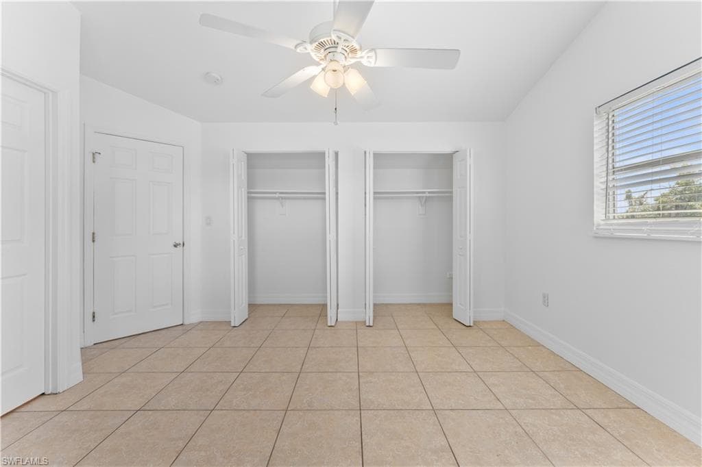 Unfurnished bedroom with multiple closets, ceiling fan, light tile patterned flooring, and baseboards