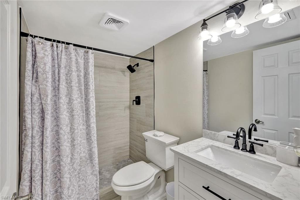Full bath featuring a tile shower, visible vents, toilet, and vanity