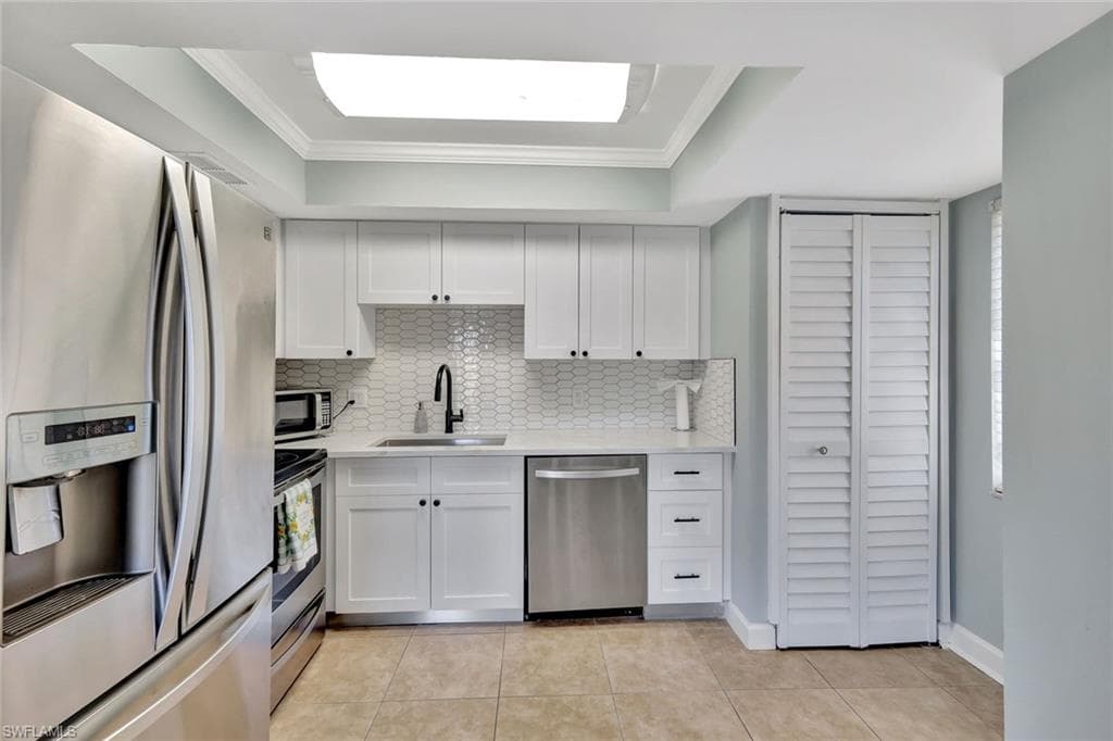 Kitchen featuring crown molding, a sink, light countertops, backsplash, and appliances with stainless steel finishes