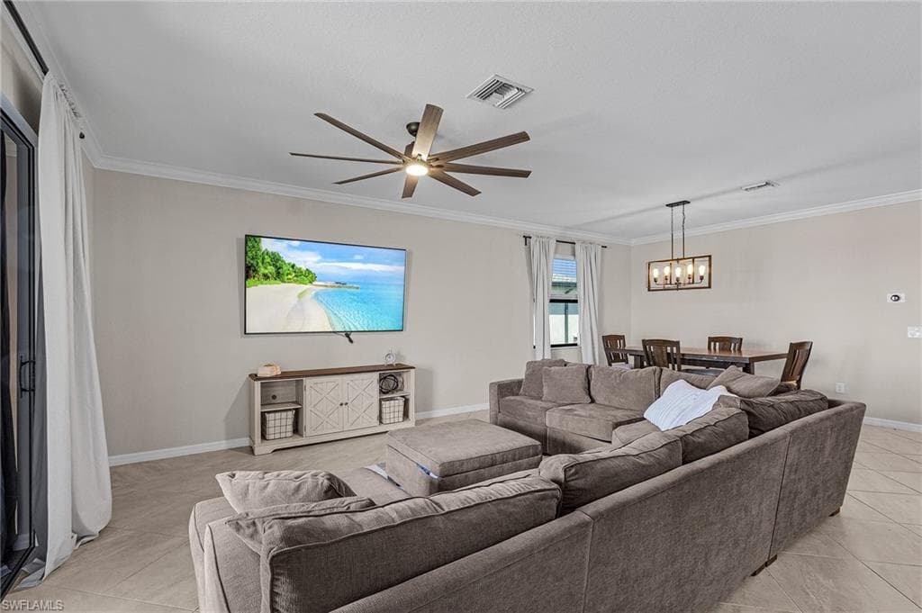 Living area featuring baseboards, crown molding, visible vents, and ceiling fan with notable chandelier