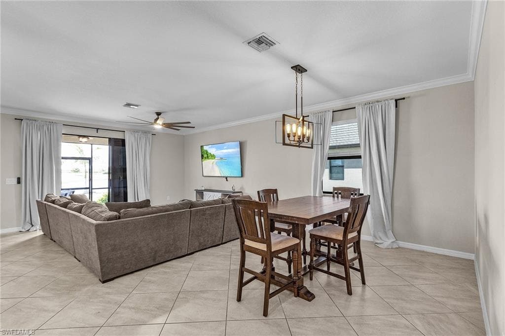Dining space featuring light tile patterned flooring, visible vents, ornamental molding, and ceiling fan with notable chandelier