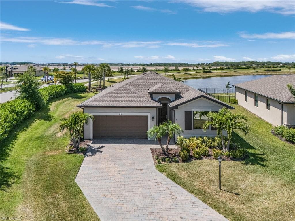 Ranch-style home featuring a front lawn, a water view, a garage, stucco siding, and decorative driveway
