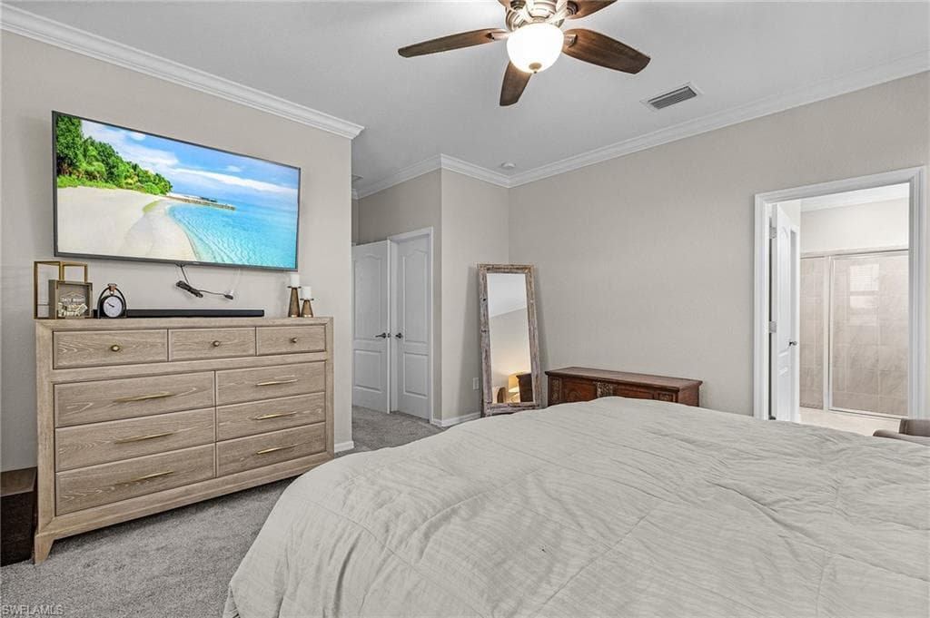 Bedroom a ceiling fan, crown molding, light colored carpet, and ensuite bathroom