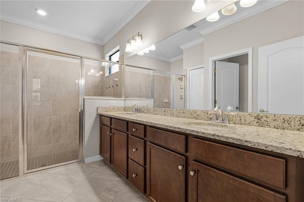 Bathroom featuring crown molding, a sink, double vanity, and a stall shower