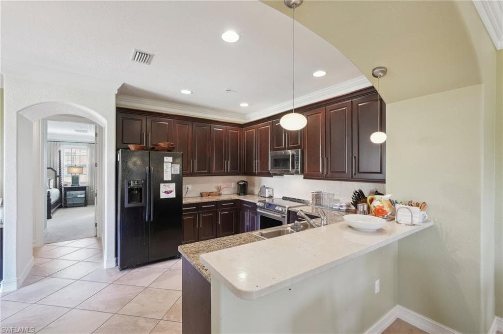 Kitchen featuring visible vents, a peninsula, dark brown cabinetry, arched walkways, and stainless steel appliances